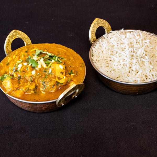 Indian chicken curry with paneer and cilantro, served with white rice in brass bowls.