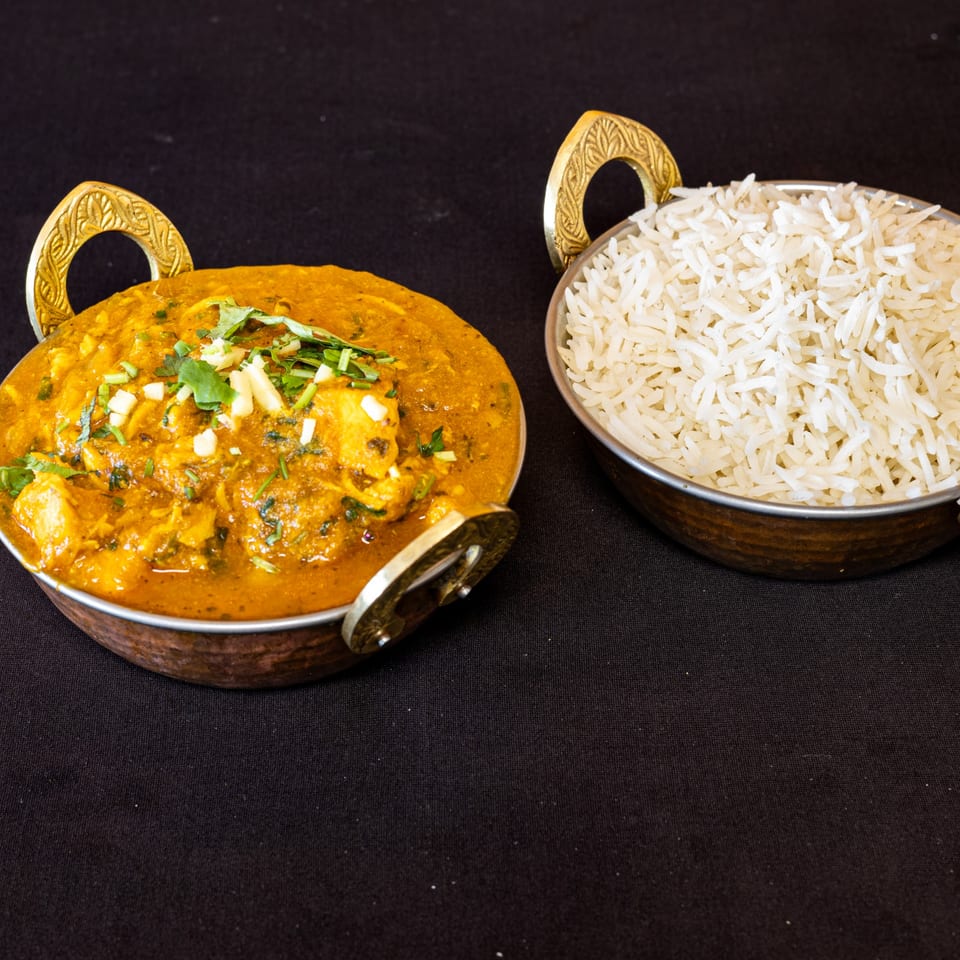 Indian chicken curry with paneer and cilantro, served with white rice in brass bowls.