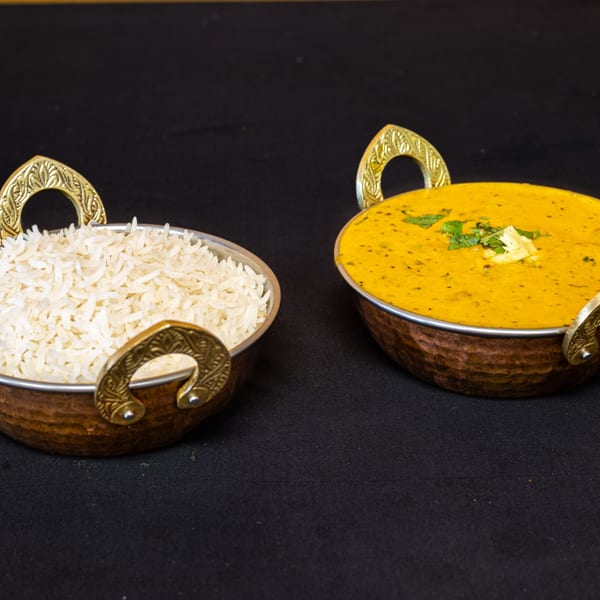 Two copper bowls, one with white rice and the other with yellow dal, on a black tablecloth.