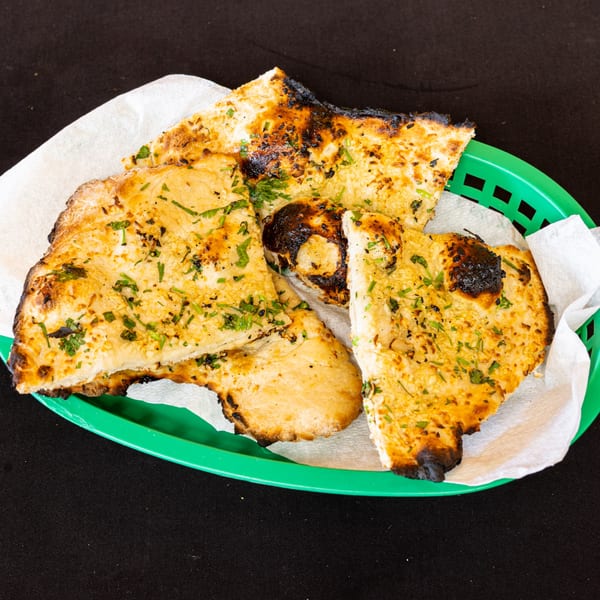 Golden-brown naan bread, garnished with herbs, served in a green basket lined with white paper.
