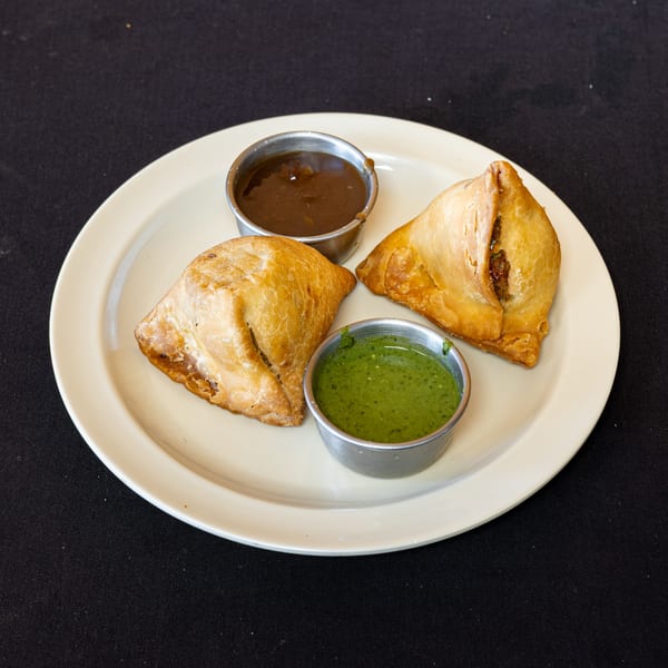 Two golden-brown samosas with green chutney and tamarind sauce on a white plate.